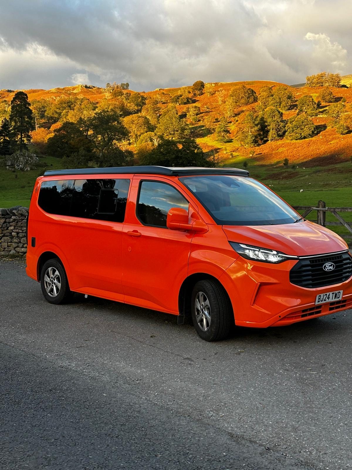Orange JMC campervan in front of autumn hills